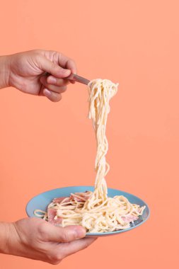 Turuncu arka planda izole edilmiş yeşil bir tabakta, çatallı kremalı spagetti yiyen. İtalyan yemeği, İtalyan mutfağı, erişte..