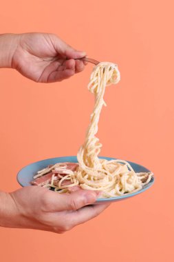 Turuncu arka planda izole edilmiş yeşil bir tabakta, çatallı kremalı spagetti yiyen. İtalyan yemeği, İtalyan mutfağı, erişte..