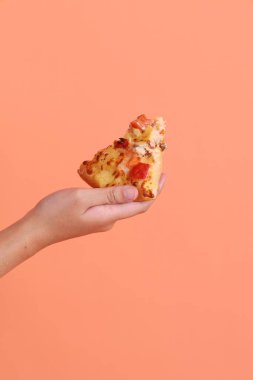 Elinde bir dilim Hawaii pizzası, üzerinde domates sosu, peynir, ananas ve domuz pastırması olan bir pizza, turuncu arka planda izole edilmiş beyaz bir tabakta. İtalyan yemeği, İtalyan mutfağı..