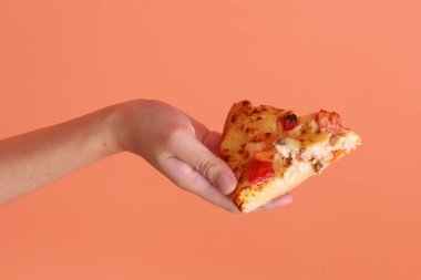 Elinde bir dilim Hawaii pizzası, üzerinde domates sosu, peynir, ananas ve domuz pastırması olan bir pizza, turuncu arka planda izole edilmiş beyaz bir tabakta. İtalyan yemeği, İtalyan mutfağı..