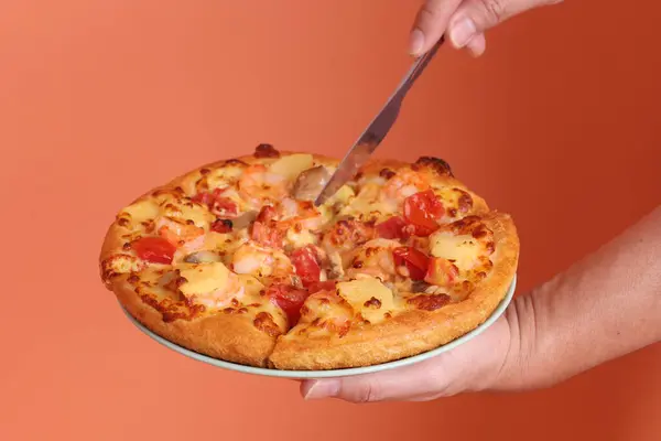 Bütün bir Hawaii pizzasını kesmek için bir bıçak, domates soslu bir pizza, peynir, ananas ve beyaz bir tabakta jambon ya da domuz pastırması, turuncu bir zeminde izole edilmiş. İtalyan yemeği, İtalyan mutfağı..