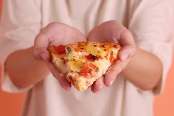 Elinde bir dilim Hawaii pizzası, üzerinde domates sosu, peynir, ananas ve domuz pastırması olan bir pizza, turuncu arka planda izole edilmiş beyaz bir tabakta. İtalyan yemeği, İtalyan mutfağı..