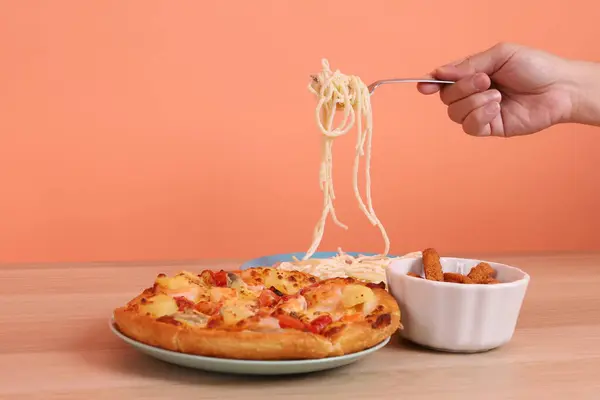 Turuncu arka planda izole edilmiş Hawaii pizzası ve tavuk çubuklarıyla kremalı spagetti yiyen bir el. İtalyan yemeği, İtalyan mutfağı..