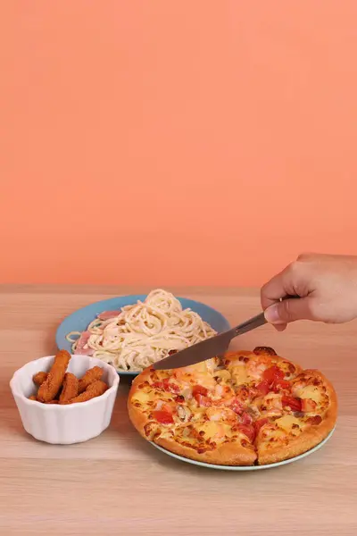 Turuncu arka planda izole edilmiş Hawaii pizzası ve tavuk çubuklarıyla kremalı spagetti yiyen bir el. İtalyan yemeği, İtalyan mutfağı..