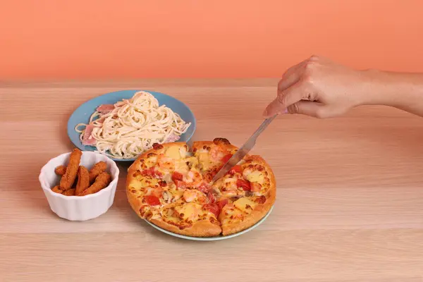 Turuncu arka planda izole edilmiş Hawaii pizzası ve tavuk çubuklarıyla kremalı spagetti yiyen bir el. İtalyan yemeği, İtalyan mutfağı..
