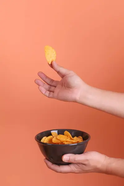 Elinde patates cipsi olan siyah bir kase, turuncu arka planda izole edilmiş. abur cubur, abur cubur, fast food, stüdyo.