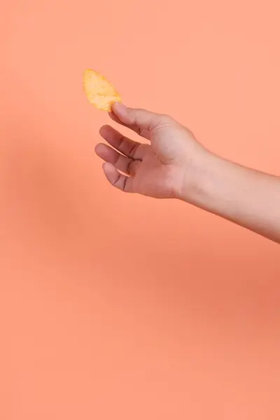 Elinde turuncu bir arka planda izole edilmiş patates cipsi var. Abur cubur, abur cubur, fast food, stüdyo.