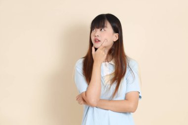 Açık mavi polo tişörtlü, beyaz şortlu, bej arkaplanlı genç bir Asyalı kadının orta boy fotoğrafı. Üniversite öğrencisi, Gen Z