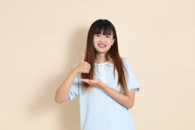 Orta boy Asyalı bir kadının açık mavi polo tişörtü ve beyaz şort giydiği bir fotoğraf. Başparmaklar yukarı, tamam mı? Ya da bej bir arka plan. Üniversite öğrencisi, Gen Z