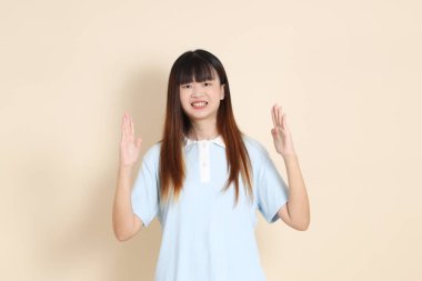 Orta boy Asyalı bir kadının açık mavi polo tişörtü ve beyaz şortu, Ölçü Sembolü, küçük, büyük, düz bir bej arka plan ile orta boy fotoğrafı. Üniversite öğrencisi, Gen Z