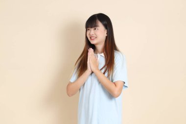 Açık mavi polo tişörtlü, beyaz şortlu, bej arka planda selamlaşan orta boy bir Asyalı kadın resmi. Üniversite öğrencisi, Gen Z