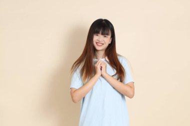 Açık mavi polo tişört giyen genç bir Asyalı kadın ve beyaz şort giymiş, bej bir arka planda dua ve huzur ederken orta boy bir fotoğraf. Üniversite öğrencisi, Gen Z