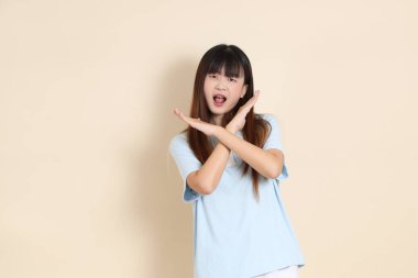 Açık mavi polo tişörtlü, beyaz şortlu genç bir Asyalı kadın, dur, reddediyor, düz bir bej arka plana hayır diyor. Üniversite öğrencisi, Gen Z, Summer