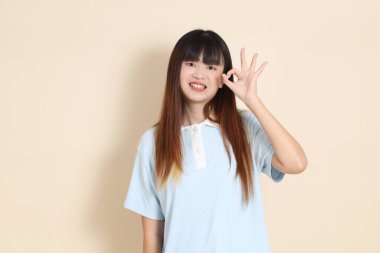 Açık mavi polo tişörtlü genç bir Asyalı kadın ve beyaz şortlu, baş parmakları havada, tamam mı? Üniversite öğrencisi, Gen Z, Summer