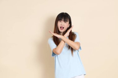 Açık mavi polo tişörtlü, beyaz şortlu genç bir Asyalı kadın, dur, reddediyor, düz bir bej arka plana hayır diyor. Üniversite öğrencisi, Gen Z, Summer
