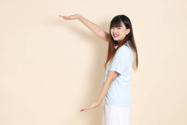 Açık mavi polo tişört giyen genç bir Asyalı kadın ve beyaz şort, Ölçü Sembolü, Küçük, Büyük, düz bir bej arka plan. Üniversite öğrencisi, Gen Z, Summer