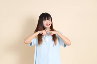 Açık mavi polo tişörtlü, beyaz şortlu genç bir Asyalı kadın, dur, reddediyor, düz bir bej arka plana hayır diyor. Üniversite öğrencisi, Gen Z, Summer