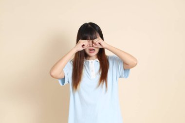 Açık mavi polo tişörtlü genç bir Asyalı kadın ve beyaz şortlu, hayal kırıklığına uğramış, bej bir arka planda ağlayan. Üniversite öğrencisi, Gen Z, Summer