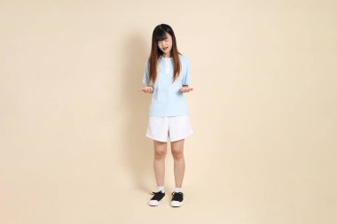 Açık mavi polo tişört giyen genç Asyalı kadın ve beyaz şort, Yazık, bej arka planda hayal kırıklığına uğramış. Üniversite öğrencisi, Gen Z, Summer