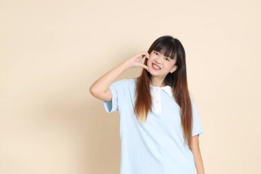 Açık mavi polo tişörtlü genç bir Asyalı kadın, ve beyaz şort, kalp şeklinde, mini kalp, düz bir bej arka planda aşk. Üniversite öğrencisi, Gen Z, Summer