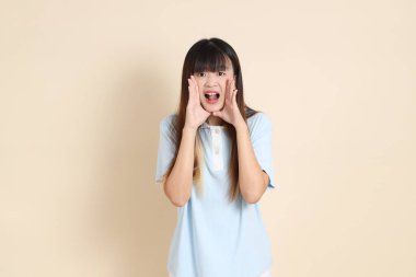 Açık mavi polo tişörtlü, beyaz şortlu, bağıran, bej arka planda megafon tutan genç bir Asyalı kadın. Üniversite öğrencisi, Gen Z, Summer