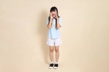 Açık mavi polo tişörtlü, beyaz şortlu, bağıran, bej arka planda megafon tutan genç bir Asyalı kadın. Üniversite öğrencisi, Gen Z, Summer