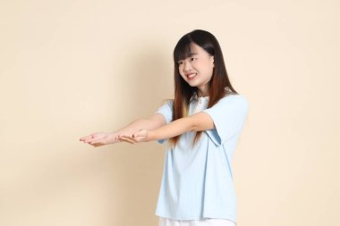 Açık mavi polo tişörtlü, beyaz şortlu genç bir Asyalı kadın bej arka planda alış-veriş yapıyor. Üniversite öğrencisi, Gen Z, Summer