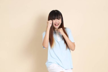 Açık mavi polo tişörtlü, beyaz şortlu genç bir Asyalı kadın bej bir arka plana karşı savaşıyor. Üniversite öğrencisi, Gen Z, Summer