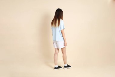 Açık mavi polo tişörtlü, beyaz şortlu, bej arka planda yürüyen genç Asyalı bir kadın. Üniversite öğrencisi, Gen Z, Summer