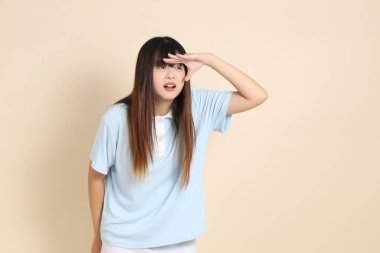 Açık mavi polo tişörtlü genç bir Asyalı kadın, ve beyaz şortlu, uzaktan bakan, düz bir bej arka plana bakan. Üniversite öğrencisi, Gen Z, Summer