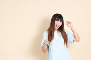 Açık mavi polo tişörtlü, beyaz şortlu, bej arka planda dans eden genç Asyalı bir kadın. Üniversite öğrencisi, Gen Z, Summer