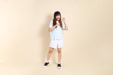 Açık mavi polo tişörtlü, beyaz şortlu, bej arka planda dans eden genç Asyalı bir kadın. Üniversite öğrencisi, Gen Z, Summer