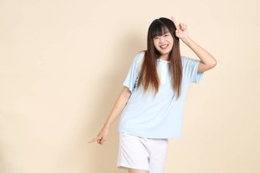 Açık mavi polo tişörtlü, beyaz şortlu, bej arka planda dans eden genç Asyalı bir kadın. Üniversite öğrencisi, Gen Z, Summer