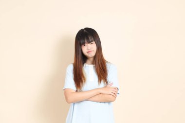 Açık mavi polo tişörtlü genç bir Asyalı kadın, ve beyaz şortlu, baş ağrısı ya da stresi olan düz bir bej arka plan. Üniversite öğrencisi, Gen Z, Summer