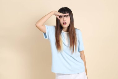Açık mavi polo tişörtlü genç bir Asyalı kadın, ve beyaz şortlu, uzaktan bakan, düz bir bej arka plana bakan. Üniversite öğrencisi, Gen Z, Summer