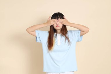 Açık mavi polo tişörtlü, beyaz şortlu, bej arka planda gözleri olan genç Asyalı bir kadın. Üniversite öğrencisi, Gen Z, Summer