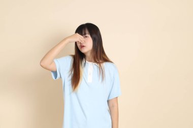 Açık mavi polo tişörtlü genç bir Asyalı kadın ve beyaz şortlu, kokulu, düz bir bej arka planda burun kaplayan. Üniversite öğrencisi, Gen Z, Summer