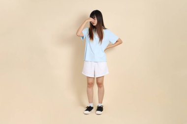 Açık mavi polo tişörtlü, beyaz şortlu, bej arka planda kusmuk olan genç bir Asyalı kadın. Üniversite öğrencisi, Gen Z, Summer