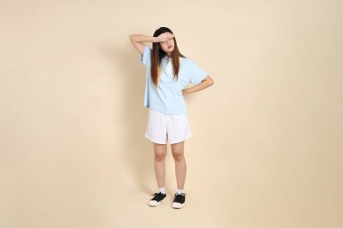 Açık mavi polo tişörtlü, beyaz şortlu, bej arka planda kusmuk olan genç bir Asyalı kadın. Üniversite öğrencisi, Gen Z, Summer