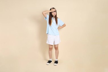 Açık mavi polo tişörtlü, beyaz şortlu, bej arka planda kusmuk olan genç bir Asyalı kadın. Üniversite öğrencisi, Gen Z, Summer