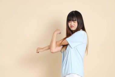 Açık mavi polo tişört giyen genç bir Asyalı kadın, ve beyaz şort, düz bir bej arka planda armache. Üniversite öğrencisi, Gen Z, Summer