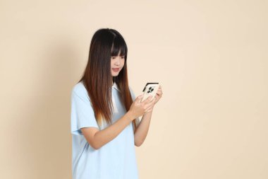 Açık mavi polo tişörtlü, beyaz şortlu genç bir Asyalı kadın, bej arka planda cep telefonlu bir kredi kartı tutuyor. Üniversite öğrencisi, Gen Z, Summer