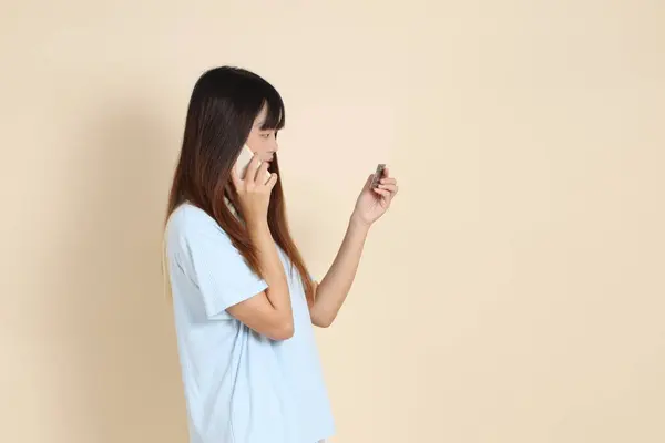 Açık mavi polo tişörtlü, beyaz şortlu genç bir Asyalı kadın, bej arka planda cep telefonlu bir kredi kartı tutuyor. Üniversite öğrencisi, Gen Z, Summer