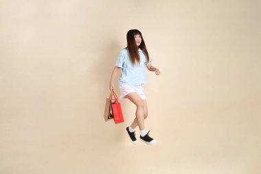 Açık mavi polo tişörtlü genç bir Asyalı kadın ve beyaz şortlu. Elinde bej arka planda bir alışveriş çantası var. Üniversite öğrencisi, Gen Z, Summer