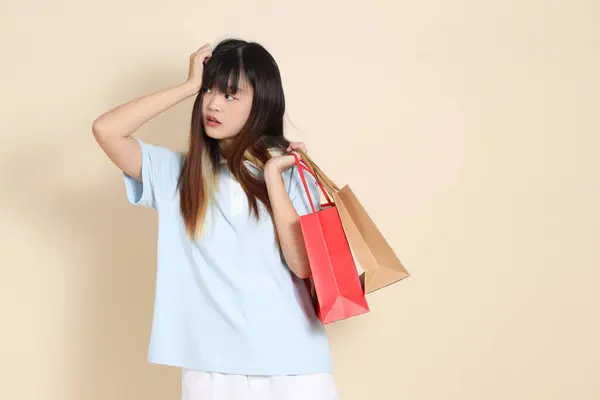 Açık mavi polo tişörtlü genç bir Asyalı kadın ve beyaz şortlu. Elinde bej arka planda bir alışveriş çantası var. Üniversite öğrencisi, Gen Z, Summer