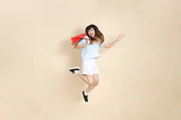 Açık mavi polo tişörtlü genç bir Asyalı kadın ve beyaz şortlu. Elinde bej arka planda bir alışveriş çantası var. Üniversite öğrencisi, Gen Z, Summer