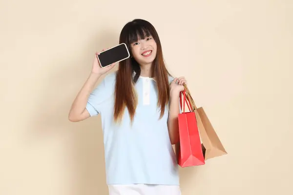 Açık mavi polo tişörtlü genç bir Asyalı kadın ve beyaz şortlu. Elinde bej arka planda bir alışveriş çantası var. Üniversite öğrencisi, Gen Z, Summer