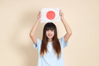 Açık mavi polo tişörtlü genç bir Asyalı kadın ve bej arka planda Japon ya da Japon bayrağı tutan beyaz şortlu. Üniversite öğrencisi, Gen Z, Summer