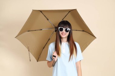 Mavi polo tişörtlü, beyaz şortlu, bej arka planda Şemsiye tutan Asyalı bir kadın. Üniversite öğrencisi, Gen Z