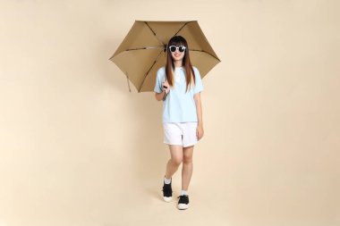 Mavi polo tişörtlü, beyaz şortlu, bej arka planda Şemsiye tutan Asyalı bir kadın. Üniversite öğrencisi, Gen Z